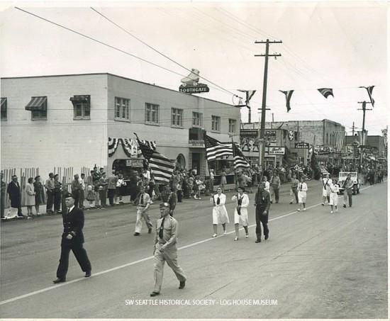 Parade in White Center, Vern Gould leading the procession down 16th Ave SW. Some of the businesses visible are the Southgate Roller Rink, Sherrill's Ice Cream, J&W Tavern, and the A&B Tavern. August 1947 SWSHS 2005.001.0665